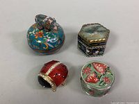 Four decorative pill boxes arranged on a white surface, showing elephant music box and three smaller boxes
