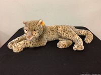 Front and side view of the Steiff plush snow leopard on a black surface illustrating size and fur details.