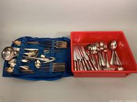 Tray with mixed patterns of Rostfrei flatware pieces, including knives, forks, spoons and serving utensils arranged in red container and blue fabric roll