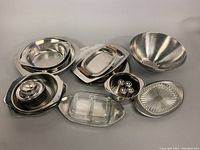 Overview of the full collection showing various stacked stainless steel bowls, a small lidded container set, rectangular trays, and a glass divided dish.