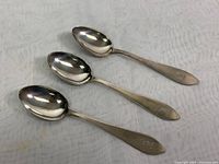 Three sterling silver Birks teaspoons laid flat showing spoons and handles with monogram engravings