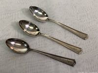 Photo showing three sterling silver teaspoons laid on a white fabric background, displaying their full length and oval bowls.