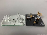 Seven Swarovski crystal figures on mirrored bases. Five animal figures: four penguins and one swan. The other set includes a clock and a champagne display with glass and stopper, all crystal with gold accents.