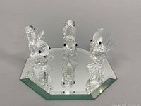 Three Swarovski crystal animal figurines on a mirrored base: two squirrels and one rooster, all faceted and clear with black eyes.