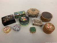 Ten trinket boxes in various materials and shapes arranged in rows: wood, metal, plastic, oval, rectangular, heart-shaped, and round boxes.