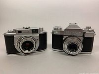 Front view of two vintage film cameras: Minolta Optiper MX on the left and Contaflex Zeiss Ikon on the right.
