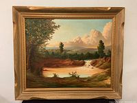 Framed oil painting showing full composition of creek or pond with trees, hills and cloudy sky.