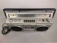 Full front view of vintage Sony stereo cassette-corder with two speakers, cassette slot, control panel, and antenna holder showing antenna broken off.