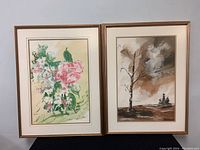 Two framed watercolour paintings, one floral and one landscape with a tree, shown side by side against a white wall.