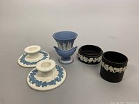 Five Wedgwood porcelain pieces including blue jasperware urn, two black jasperware holders, and two white candlesticks with blue floral reliefs.