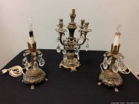 Three-piece set on black surface showing a 16-inch French Louis XVI style candelabra with crystal drops flanked by two 12-inch similar style electric lamps with hanging crystal drops.