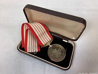 Photo of medal with ribbon inside original presentation box, showing overall presentation condition.