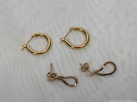 Two pairs of gold earrings (hoops and drop earrings) on white fabric