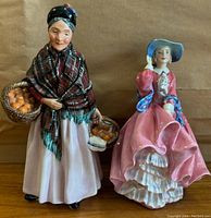 Front view of The Orange Lady and Top o' the Hill figurines side by side on brown background