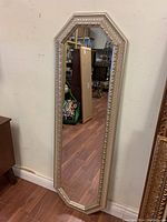 Tall 52 inch wall mirror with octagonal frame, gold-toned with decorative texture on molding, leaning against a wall showing hardwood floor and background items.