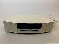 Front view of the off-white Bose Wave Music System, showing the CD slot, speaker grills, and the Bose logo.