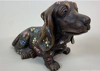 Front side view showing dachshund dog's detailed face, ears, paws and multicolored stamped floral patterns on dark brown pottery.