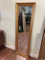 Full view of the framed rectangular mirror showing the gold textured frame and the beveled mirror surface reflecting interior room elements.