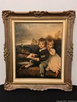 Full view of the framed print showing two children seated outdoors, in an ornate gold-toned wooden frame.