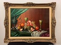 Full view of the ornately framed oil on canvas painting featuring still life with fruit, goblets, and draped green cloth.