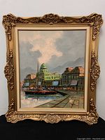 Full view of ornately carved gold-tone framed oil painting showing harbor scene with dock, boat, and buildings under cloudy sky.