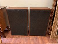 Front view of the pair of vintage wooden cabinet speakers with dark fabric grilles, showing condition and wood finish.