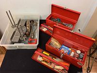 Photo showing two red metal toolboxes filled with assorted hand tools and a plastic bin containing vintage miter saw, hand plane and bow saw