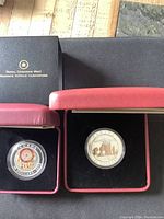 Two silver coins in red display boxes with outer black Royal Canadian Mint boxes. One coin shows colorful Dream Catcher design, the other coin depicts Hopewell Rocks scene.