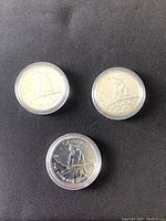 Three coins in capsules showing the cougar reverse design perched on a branch