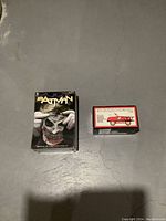 Photo showing Batman book and mask set on the left and pedal engine coin bank box on the right on a concrete floor