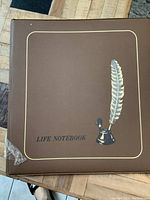 Closed brown coin album labeled 'Life Notebook' with quill graphic, showing packaging condition.