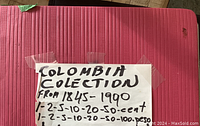 Close-up of the album cover with handwritten label detailing the Colombian coin collection from 1845-1990, the denominations included.