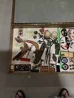 Overview of display case contents showing military medals, pins, boomerangs, toy motorcycles, jars, and various small collectible items.