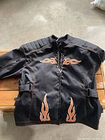 Front view of Lady Rider black motorbike jacket with orange flame designs, showing padded shoulders, zipper front, and adjustable waist straps.
