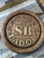 Overall front view of the round wooden tavern bar sign showing carved details, metal letters, and decorative emblem.
