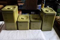 Four avocado green 1960s kitchen canisters by Harvell Kilgore arranged side by side on a white towel, showing front side with sunburst design.