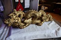 Side view of large gold-painted cast plaster dragon on cloth, showing detailed scales and curled body.