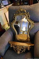 Full view of the Syroco mirror and shelf resting on a chair showing ornate gold-tone decorative frame and shelf surface.