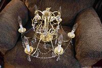 Full view of 6 light crystal chandelier with brass metal frame, white candle sleeves, clear bulbs, and crystal beads.