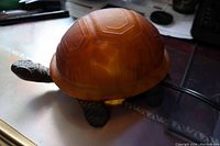 Amber glass turtle lamp from side showing glowing amber shell and metal textured head and legs.