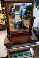 Front view of the antique Victorian walnut dresser mirror on a metal stool, showing the rectangular tilting mirror with solid wood frame and curved base.