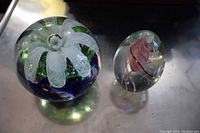 Both glass paperweights together on reflective surface showing size and design differences