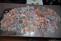 Wide overhead view showing a large scattered pile of colorful stamps on a gray surface, illustrating the volume and variety.