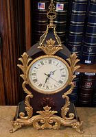 Front view of the large French style mantle clock showing clock face with Roman numerals, gold-tone metal trim, and wood body with floral inlay.