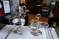 Full view of silver plate cruet with warming candle and 3-cup serving stand with glass liners displayed on a white cloth.