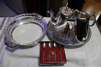 Overall view of the pie plate on holder, tea pot, milk jug, tray, and boxed spoons on table.
