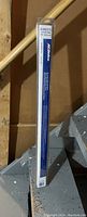 Photo of a 25 inch Anco Easy On windshield wiper blade in its original cardboard packaging, standing upright against a wooden wall and staircase.
