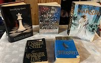 Photo of five assorted books including 'Breaking Dawn', 'The Girl Who Kicked the Hornet's Nest', 'The Chronicles of Narnia', 'No Greater Love', and 'Bittersweet'. Books show signs of light use.