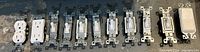Eleven assorted electrical devices including toggle switches, a rocker switch, outlets, and a blank plate, all metal-mounted.