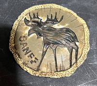 Close-up of a round wood slice with bark edges, carved with a moose and the word BANFF.